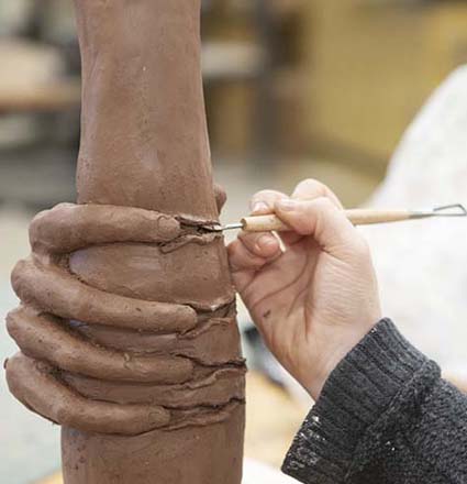 An artist sculps clay in class.