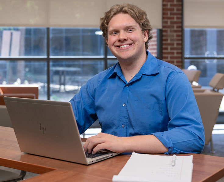 A Macomb student smailes at the camera while doing his business homework on a computer.