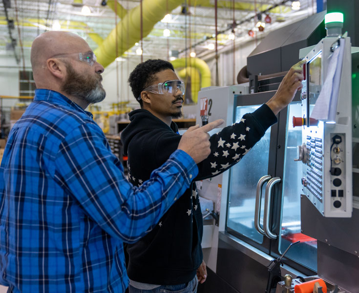 A professor teaches a Macomb student on how to use a CNC machine.