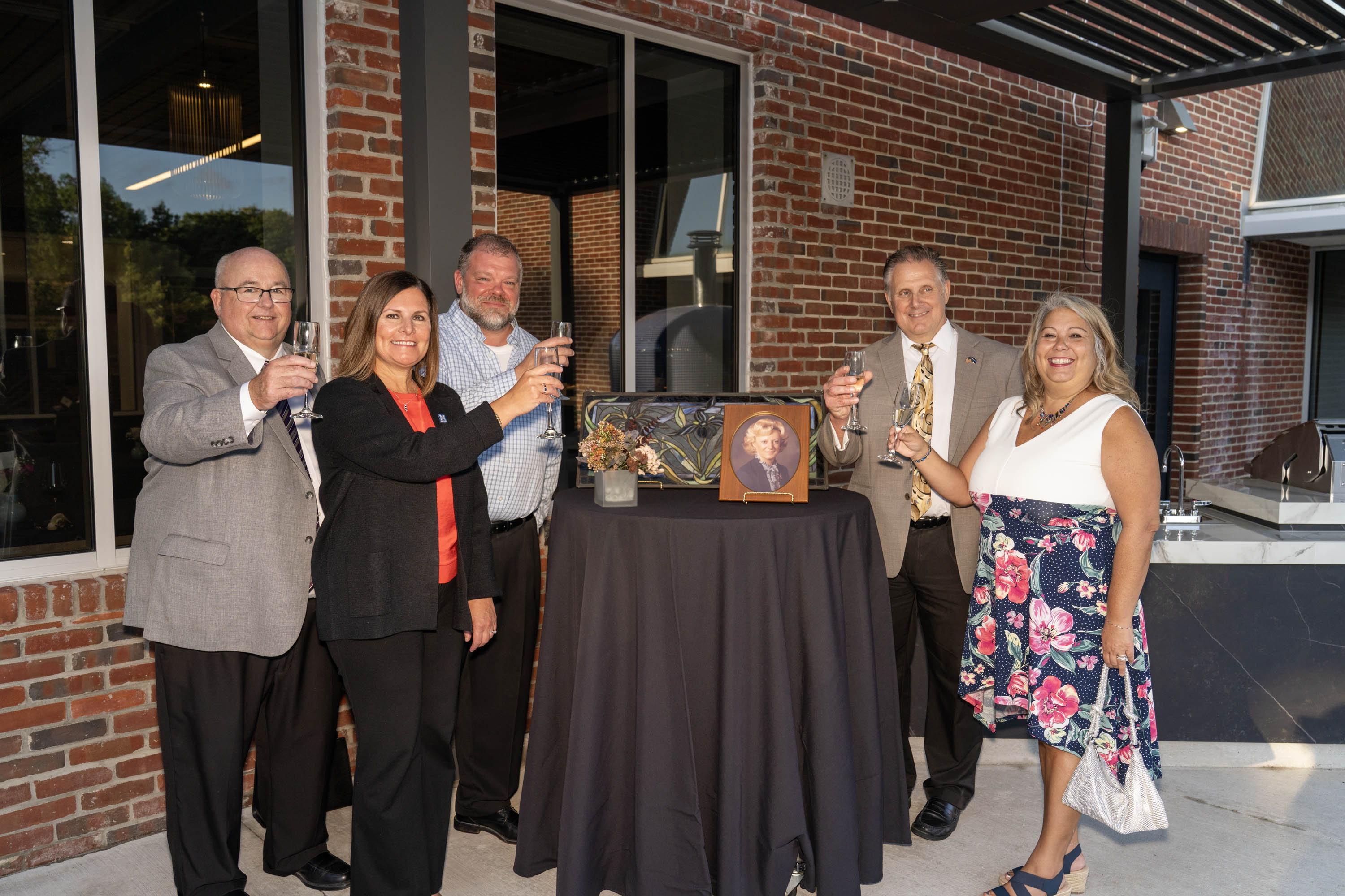 The late Shirley Glass, longtime Macomb Community College accounting professor, who left her $3.2 million estate to the college, is toasted at the dedication to her of the terrace for the renovated Monarque restaurant. From left to right: James O. Sawyer IV, president, Libby Argiri, executive vice president, Administration; Brian Newman, professor, accounting; Mike Balsamo, dean, Business, Information Technology and Culinary; and Monique Beauchamp, professor, marketing.